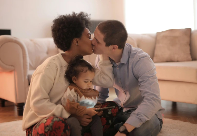 a man and woman sitting on the floor with a baby, kissing together, diverse, gen z, paul barson