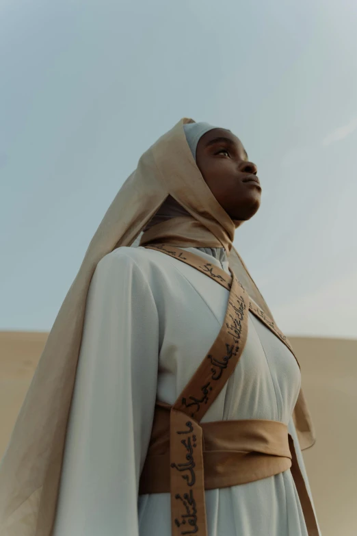 a man in a white robe standing in the desert, inspired by Thomas Blackshear, trending on pexels, afrofuturism, nun fashion model looking up, still from the mandalorian show, young middle eastern woman, in historic clothing