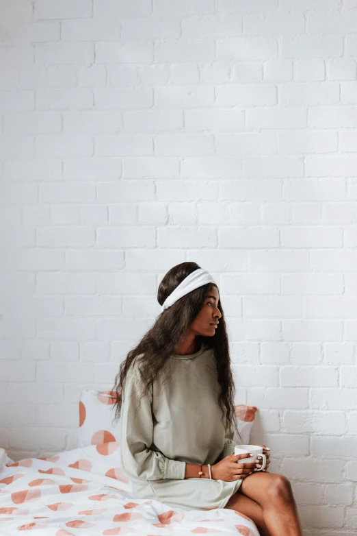 a woman sitting on top of a bed next to a white brick wall, trending on pexels, wearing a headband, girl standing, wearing a white sweater, empty background