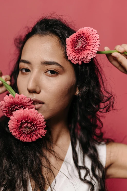 a woman holding two pink flowers in front of her face, an album cover, trending on pexels, mixed race, portrait of modern darna, made of flowers, studio photo