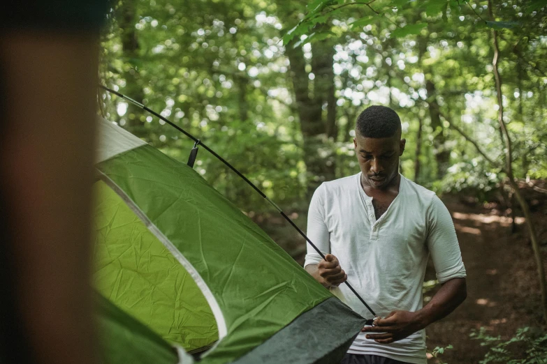 a man standing next to a green tent in the woods, happening, concentration, instagram post, hanging, adult