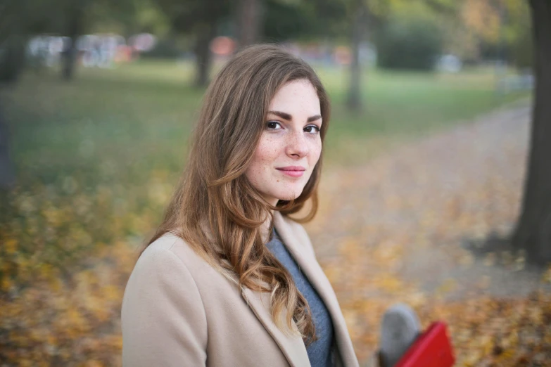 a woman holding a red book in a park, a portrait, by Alice Mason, pexels contest winner, parted light brown hair, romanian, halfbody headshot, autumnal