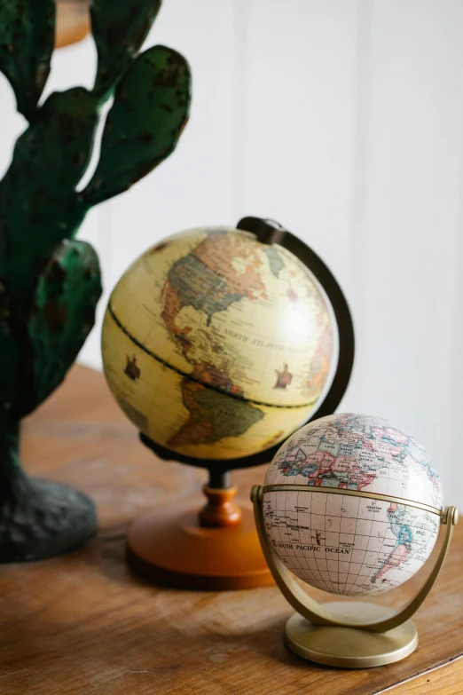 a small globe sitting on top of a wooden table, vintage inspired, various colors, woo kim, explorer