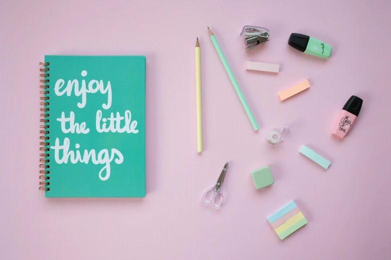 a notebook with the words enjoy the little things written on it, by Rachel Reckitt, trending on unsplash, teal studio backdrop, pink and green colour palette, miscellaneous objects, low - angle shot