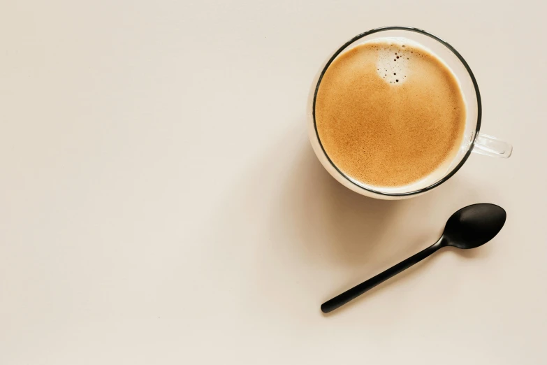 a cup of coffee and a spoon on a table, by Carey Morris, trending on unsplash, minimalism, background image, light tan, no - text no - logo, cappuccino