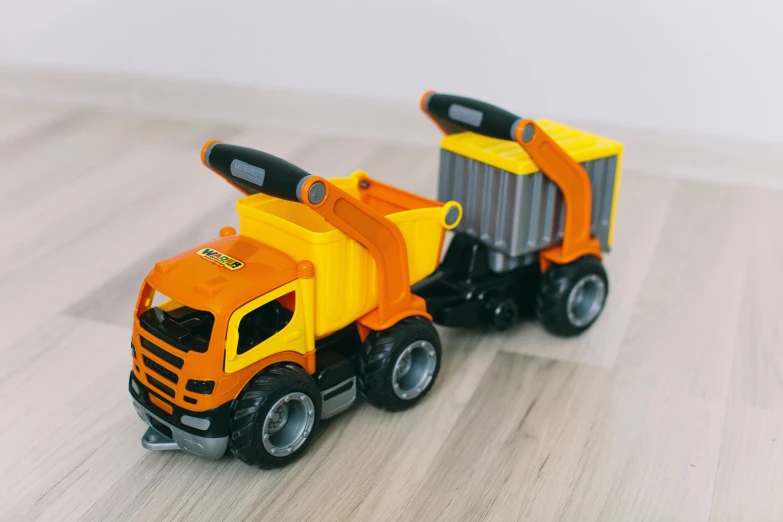 a toy truck sitting on top of a wooden floor, by Romain brook, pexels contest winner, yellow and orange color scheme, futuristic tractors, orange grey white, 🚿🗝📝