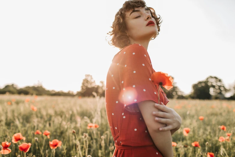 a woman standing in a field of red flowers, pexels, vintage glow, natalia dyer, sun overhead, profile image