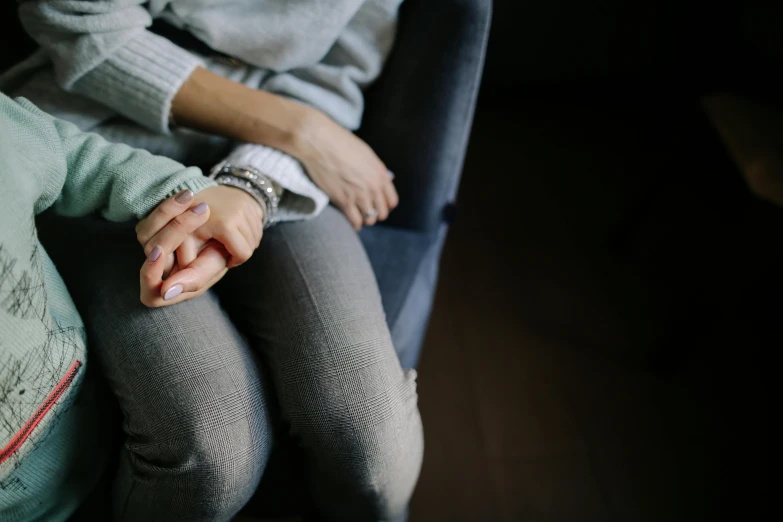 a close up of a person holding a child's hand, trending on pexels, sitting on an armchair, grey clothes, teenage girl, depressed
