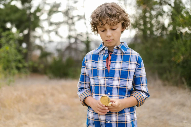 a young boy standing in a field holding a donut, by Jessie Algie, pexels, renaissance, button up shirt, gold and blue, magnifying glass, flannel