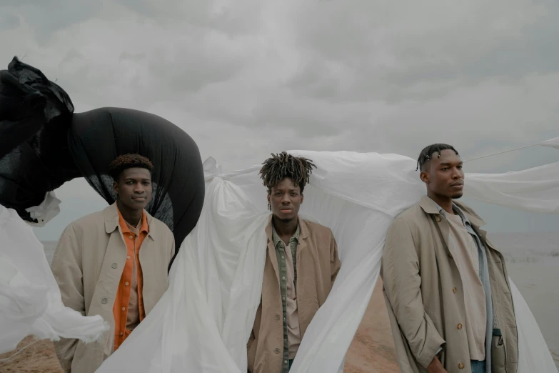 a group of three men standing next to each other, by Emma Andijewska, pexels contest winner, afrofuturism, parachutes, brown clothes, film still promotional image, cloudy