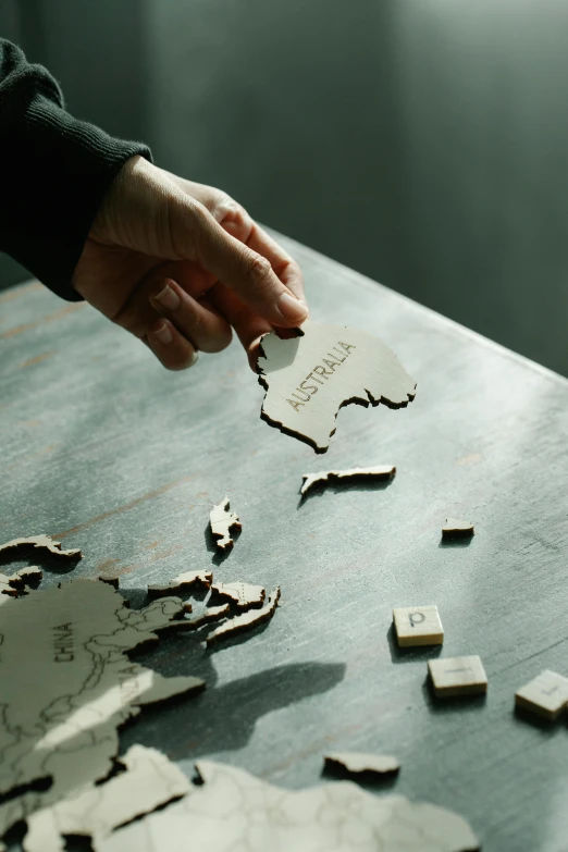 a person placing a piece of puzzle on a table, by Jessie Algie, pexels contest winner, continents, aussie, engraved, studio shot