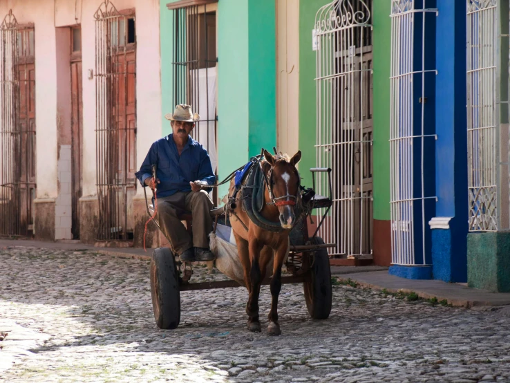 a man riding a horse drawn carriage down a cobblestone street, by Ceferí Olivé, pexels contest winner, square, caribbean, multi - coloured, che guevara