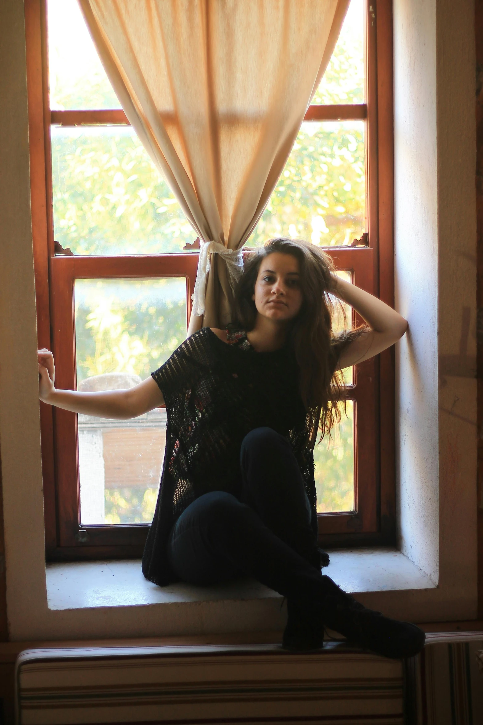a woman sitting on top of a window sill, a picture, sofya emelenko, with brown hair, dread, standing in corner of room