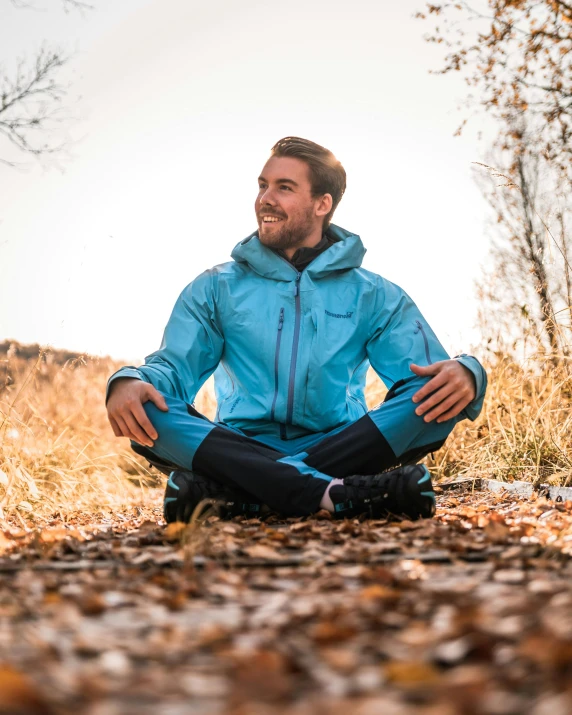 a man in a blue jacket sitting on the ground, pexels contest winner, wearing fitness gear, delightful surroundings, felix englund, smiling