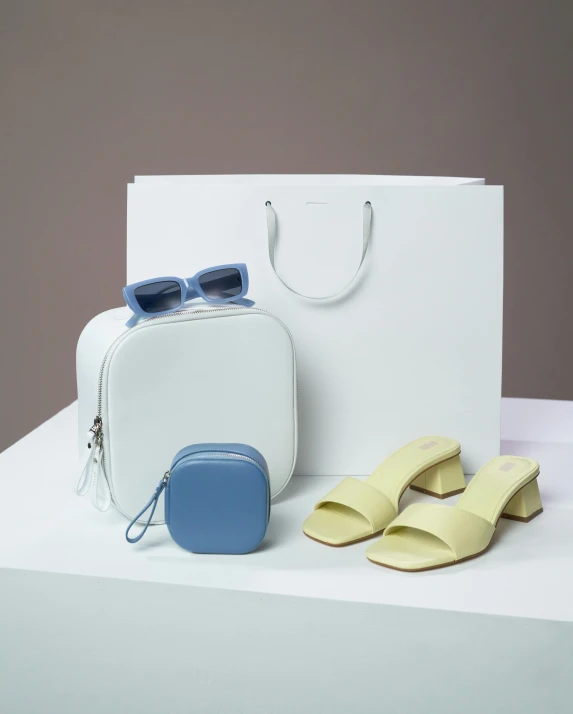 a pair of sandals and a bag on a table, inspired by Eden Box, minimalism, cream and blue color scheme, press shot, white neon, charcoal and yellow leather