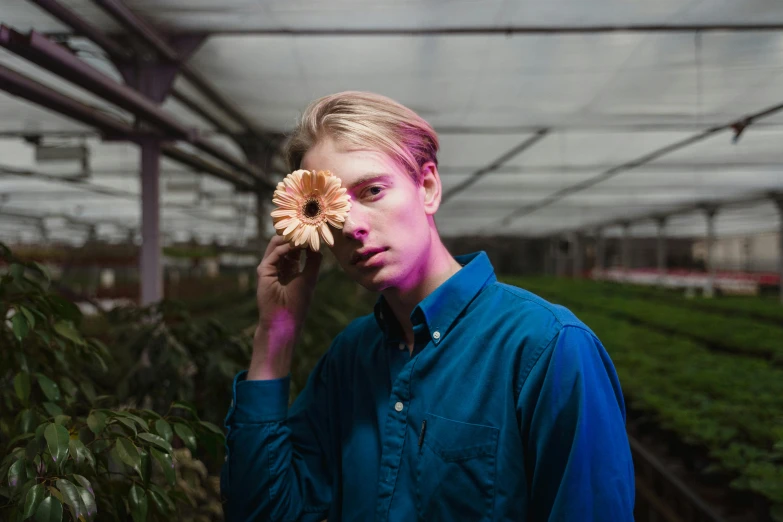 a man holding a flower in front of his face, an album cover, pexels contest winner, aestheticism, caspar david, greenhouse, serious lighting, a blond