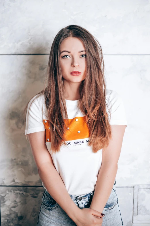 a woman leaning against a wall with her hands on her hips, an album cover, inspired by Louisa Matthíasdóttir, pexels contest winner, wearing an orange t shirt, mackenzie foy, white t-shirt, headshot profile picture