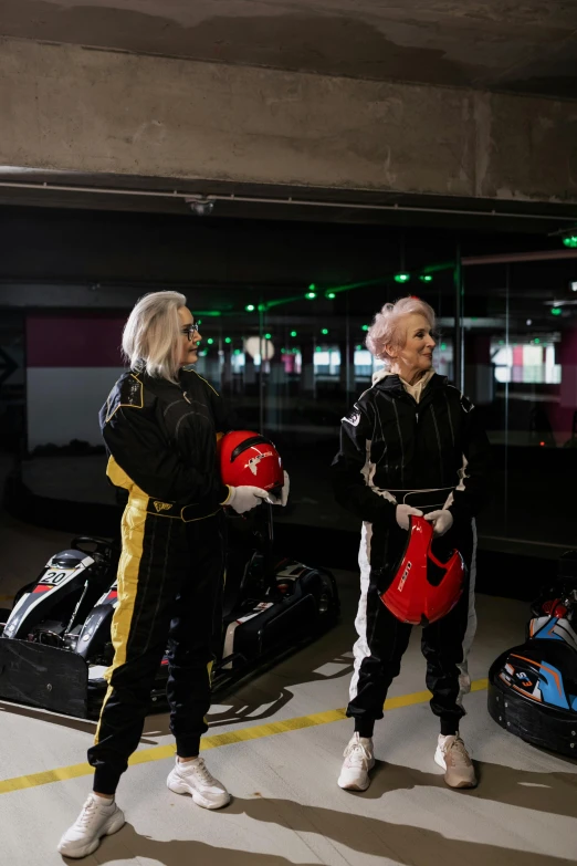 two women standing next to each other in a parking garage, inspired by Hendrick Cornelisz Vroom, happening, at racer track, wearing black and purple robes, bumper cars, two old people