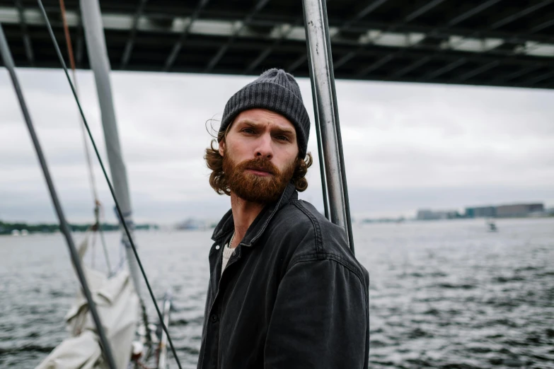 a man with a beard standing on a boat, a portrait, by Tom Bonson, pexels contest winner, beanie, with slight stubble, promotional image, blake rottinge