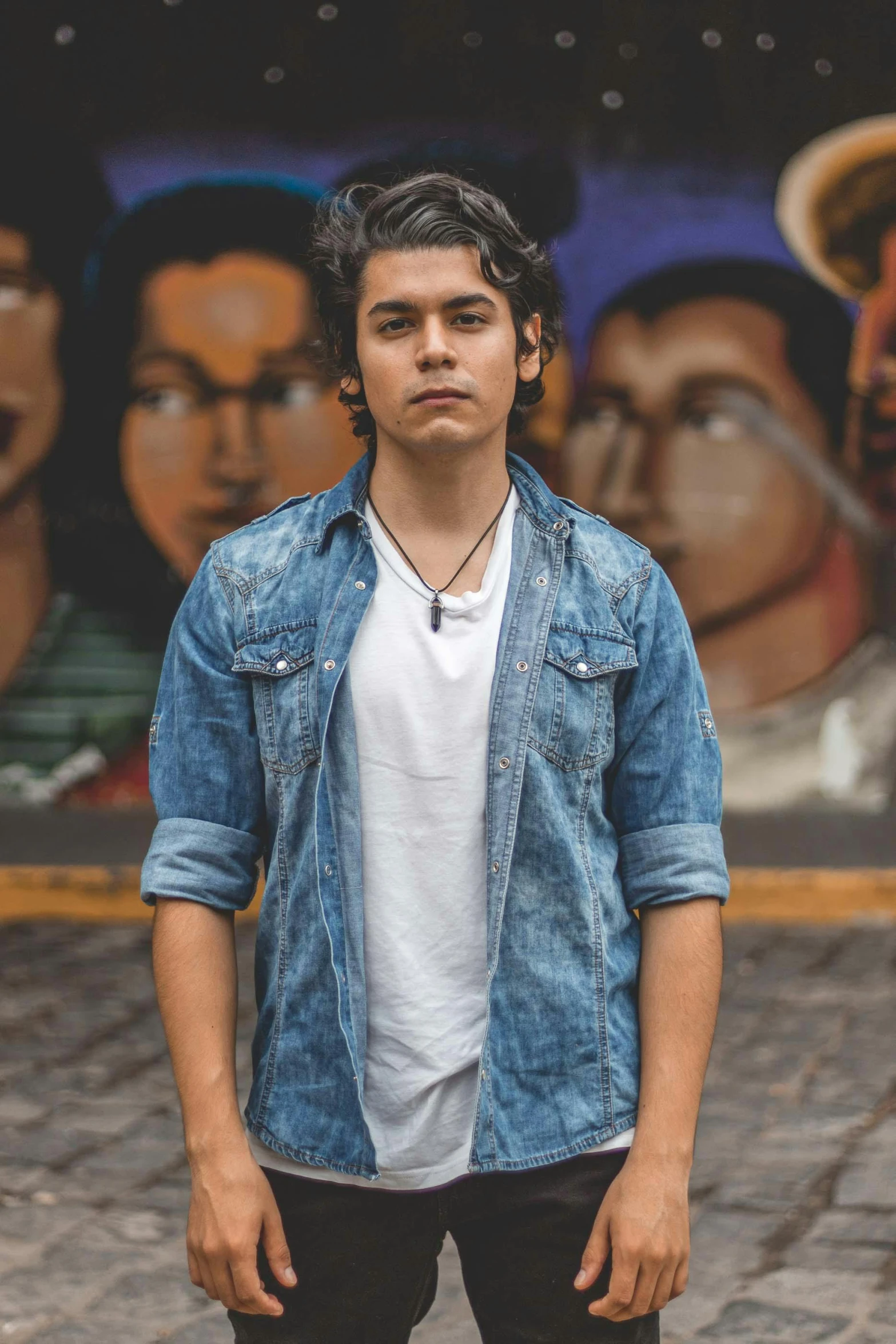 a young man standing in front of a mural, an album cover, by Alejandro Obregón, pexels, wearing a jeans jackets, headshot profile picture, concert photo, asher duran
