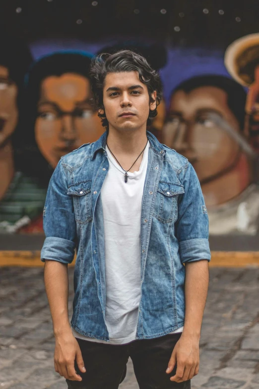 a young man standing in front of a mural, an album cover, by Alejandro Obregón, pexels, wearing a jeans jackets, headshot profile picture, concert photo, asher duran