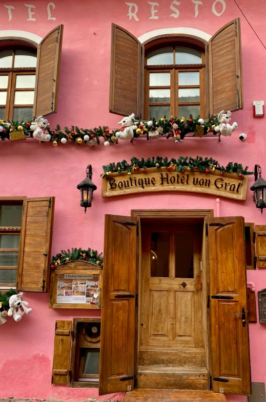 a pink building with wooden shutters and windows, inspired by Limbourg brothers, festive atmosphere, cosy