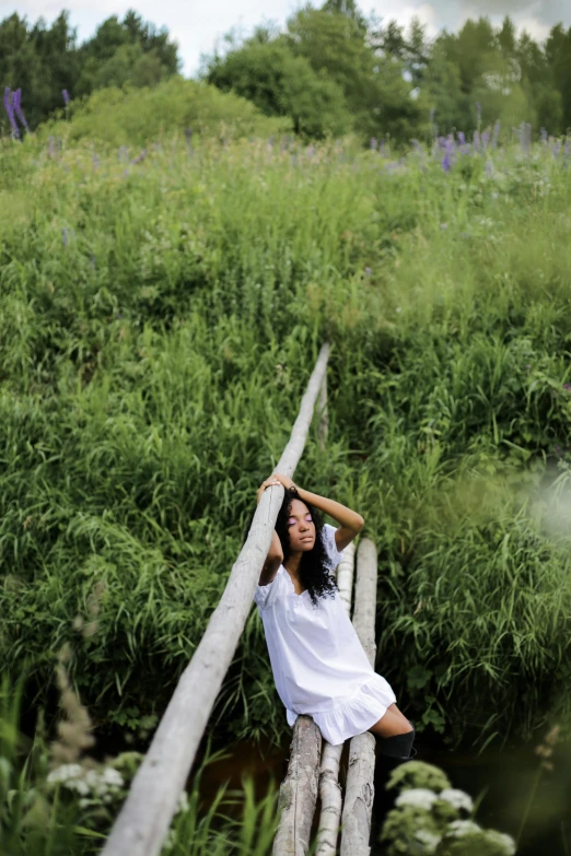 a woman in a white dress sitting on a wooden bridge, inspired by Andrew Wyeth, unsplash, laying down in the grass, mongolia, low quality photo, high angle