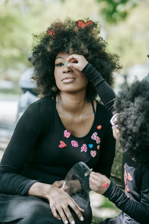 two women sitting on a bench with a dog, by Lily Delissa Joseph, trending on pexels, black arts movement, children playing with pogs, putting makeup on, long wild black curly hair, face painting