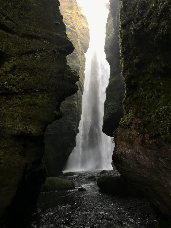 a person standing in front of a waterfall, inside a gorge, photo taken in 2018, tears running down, from the distance