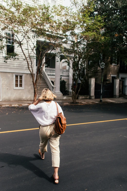 a woman walking down a street with a backpack on her back, inspired by Ruth Orkin, trending on unsplash, in savannah, ignant, khakis, in front of the house