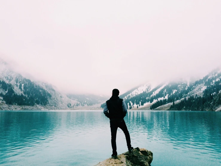 a person standing on a rock in front of a body of water, pexels contest winner, cold colours, college, carson ellis, saying