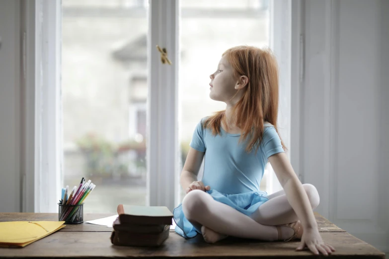 a little girl sitting on a desk in front of a window, inspired by Elizabeth Polunin, pexels contest winner, arabesque, padmasana, cute young redhead girl, tiny person watching, blue