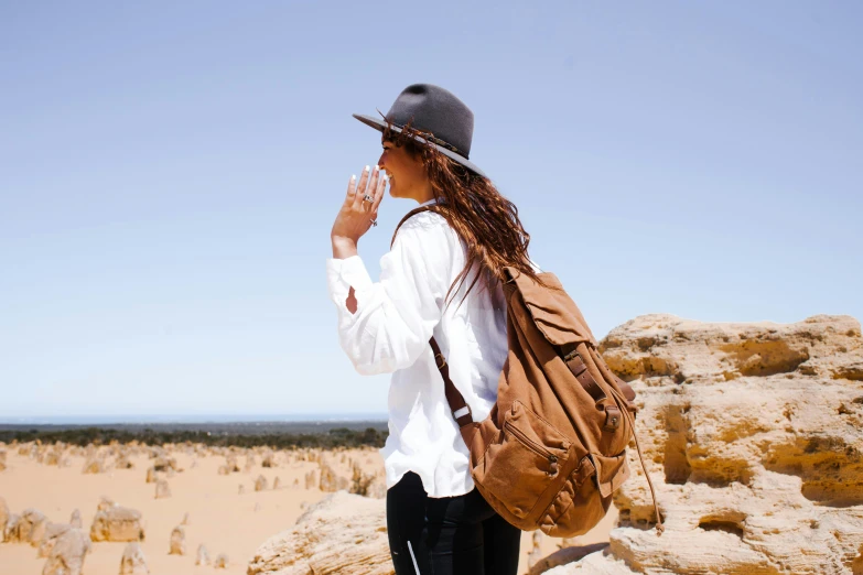 a woman standing on top of a rocky hill, pexels contest winner, renaissance, aboriginal australian hipster, sand and desert environment, a backpack, drinking