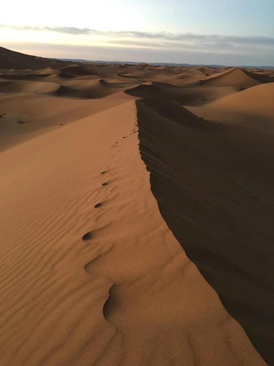 a large sand dune in the middle of a desert, pexels contest winner, footprints in the sand, it's getting dark, moroccan, looking partly to the left