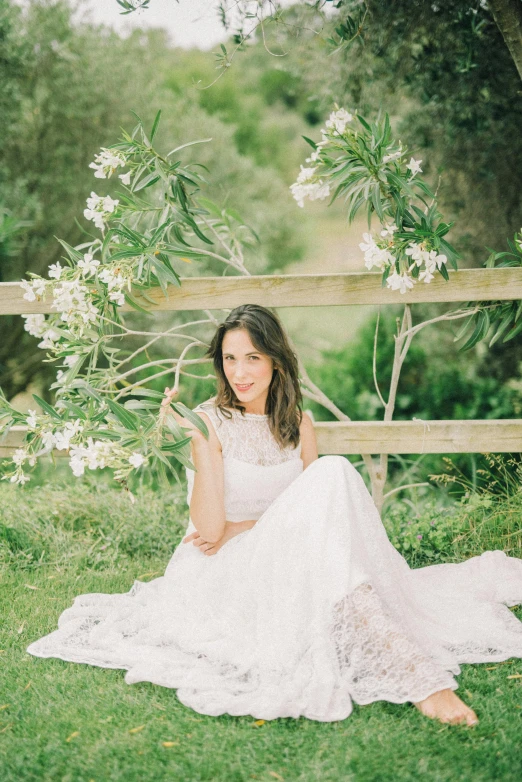 a woman sitting on top of a lush green field, in wedding dresses, manuka, in front of white back drop, sitting on a curly branch