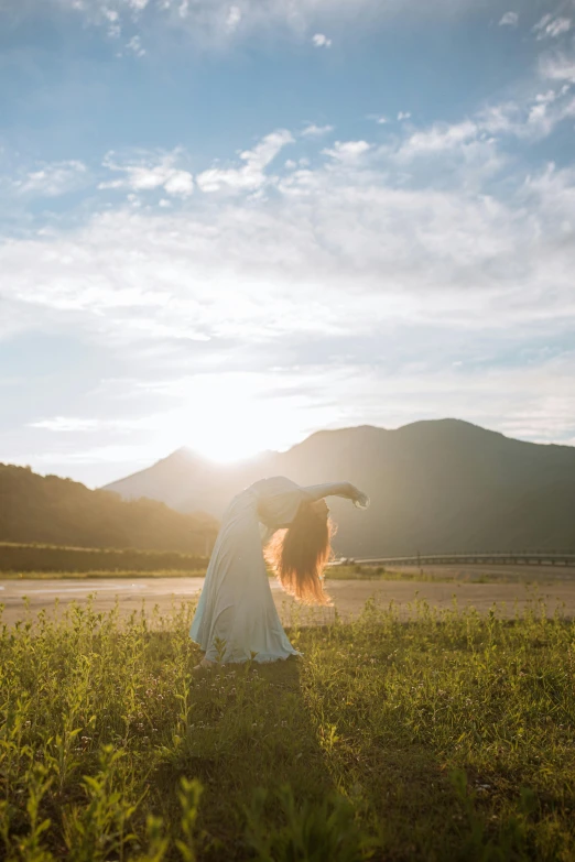 a woman standing on top of a lush green field, inspired by Ren Hang, unsplash, arabesque, sunset in a valley, brunette fairy woman stretching, taiwan, sunlit