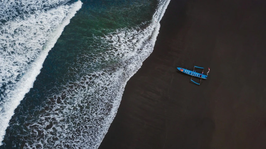 a boat sitting on top of a beach next to the ocean, by Julia Pishtar, pexels contest winner, hurufiyya, black sand, airborne view, blue, ignant