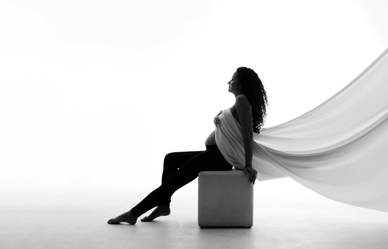 a black and white photo of a pregnant woman, a black and white photo, by Clifford Ross, pexels, art photography, with screens and silks, sitting dynamic pose, profile photography, white backdrop