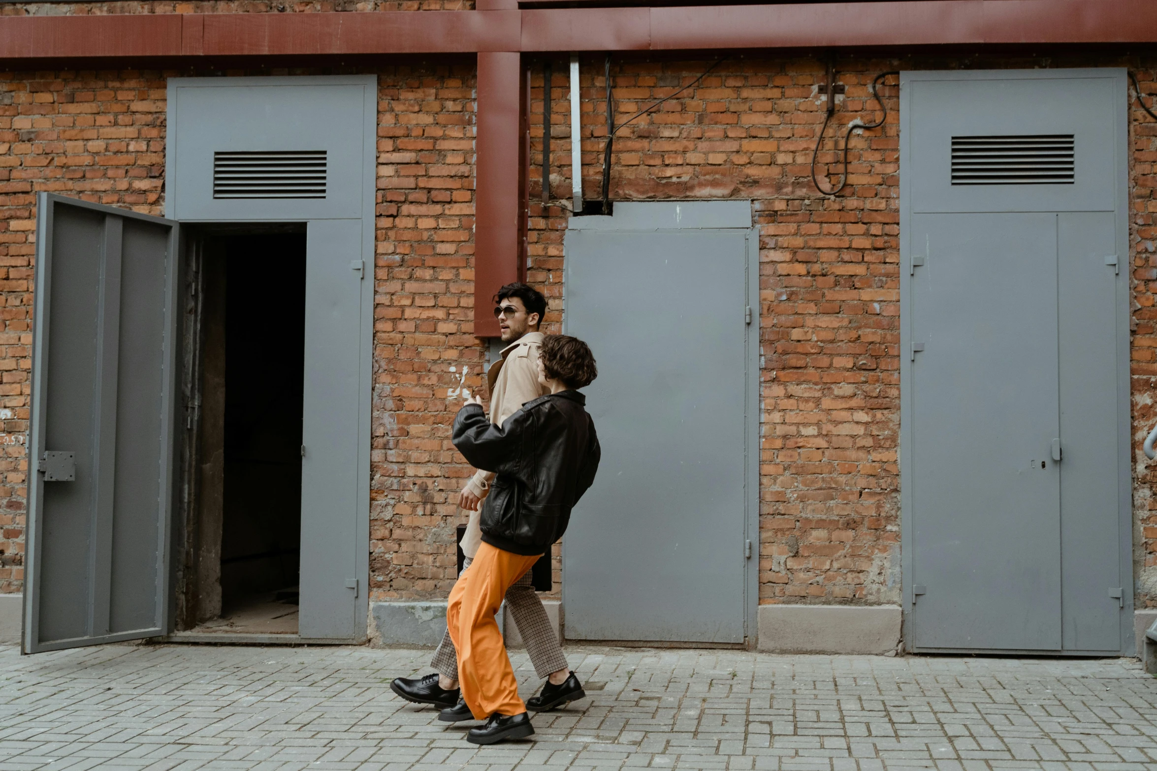 a couple of people that are standing in front of a building, by Attila Meszlenyi, trending on pexels, brown clothes, alleys, non-binary, walking boy