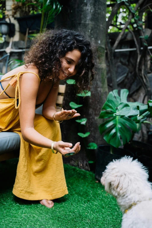 a woman sitting on a bench next to a white dog, pexels contest winner, wavy hair yellow theme, permaculture, bali, partially cupping her hands