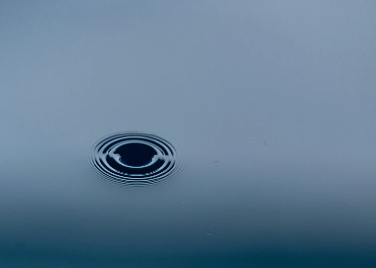 a circular object floating on top of a body of water, a microscopic photo, inspired by Lucio Fontana, pexels contest winner, minimalism, just after rain, water pipe, blue gray, black hole