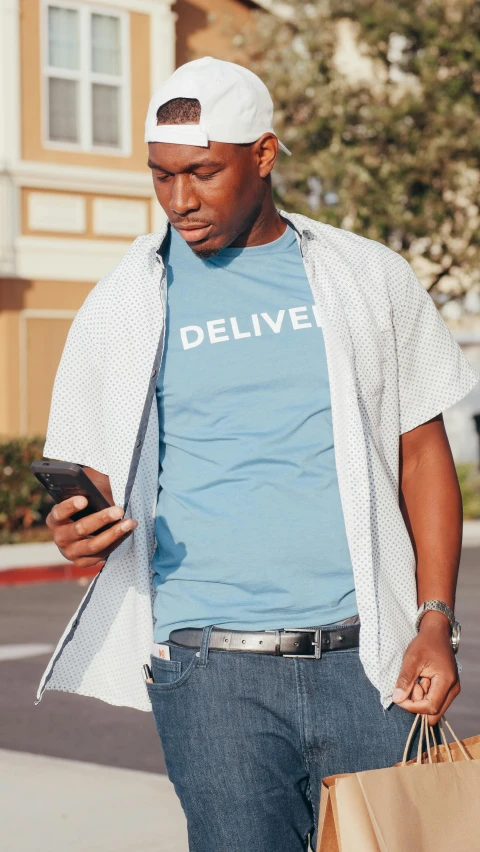 a man walking down the street with a bag and cell phone, an album cover, trending on pexels, blue tight tshirt, logo for lunch delivery, dokev, modeled