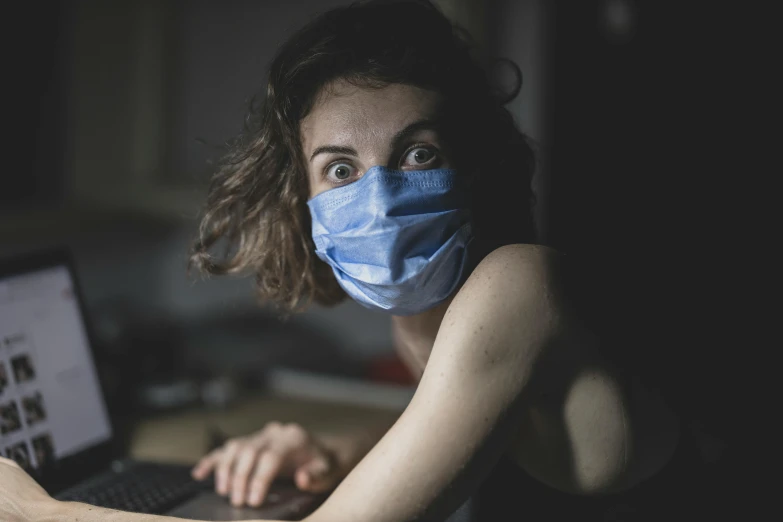 a woman wearing a face mask sitting in front of a laptop, a portrait, by Adam Marczyński, trending on pexels, happening, from horror movies, avatar image, nursing, thumbnail