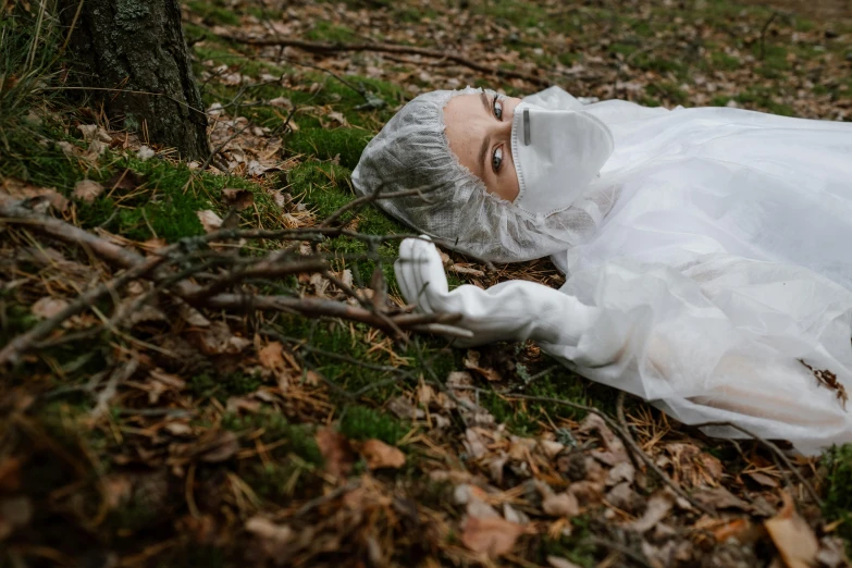 a woman in a white dress laying on the ground, wearing white silk hood, the horror in the woods, one single man in a hazmat suit, promo image