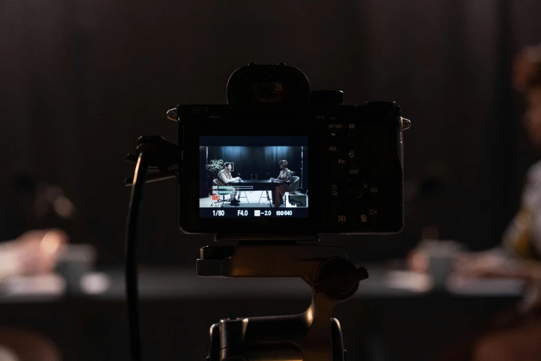 a close up of a camera on a tripod, video art, 3 actors on stage, sony a 7 siii, center focus on table, on a dark background