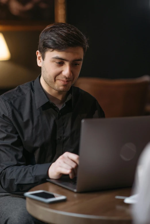 a man sitting at a table working on a laptop, pexels contest winner, wearing a black shirt, medium shot of two characters, networking, low quality photo