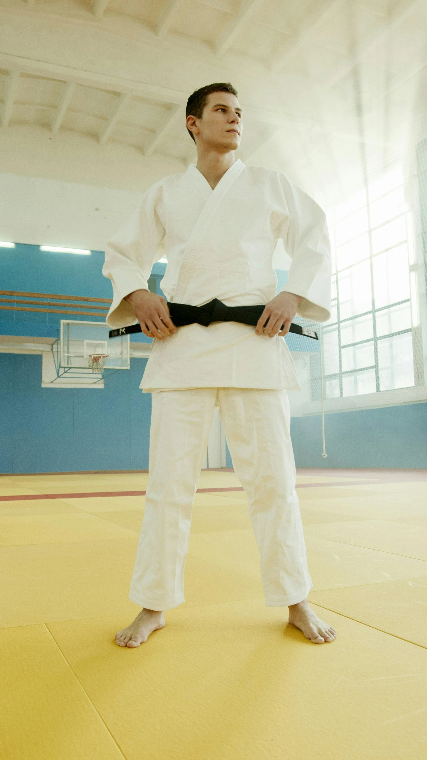 a man standing in a gym holding a black belt, by John Murdoch, japan, square, no cropping, wearing a white gi