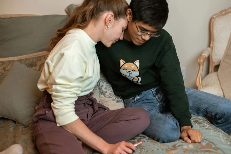 a couple of people sitting on top of a bed, trending on pexels, wearing a green sweater, teenage boy, supportive, asian female