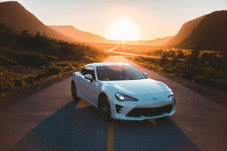 a white sports car driving down a road at sunset, pexels contest winner, avatar image, instagram picture, ae 8 6, hills in the background