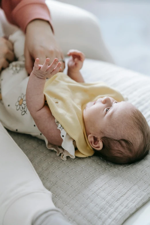 a woman holding a baby on top of a bed, unsplash, white and yellow scheme, laying down with wrists together, manuka, lightly dressed